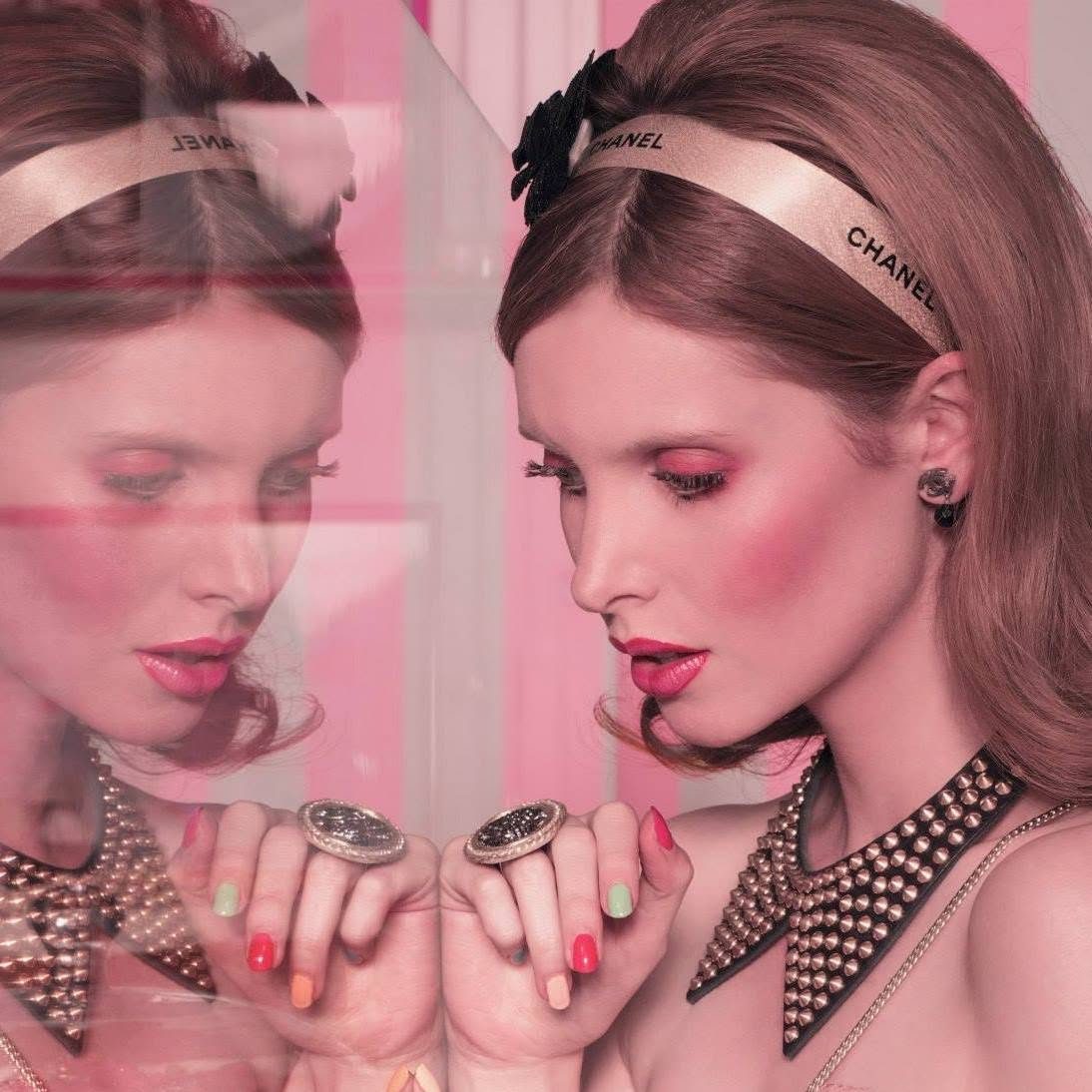 Due modelle allo specchio con cerchietto Chanel, blush rosa e labbra corallo in un editorial dai toni pastello